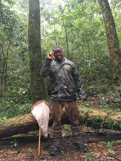 Man stands in front of a log of wood in a forest